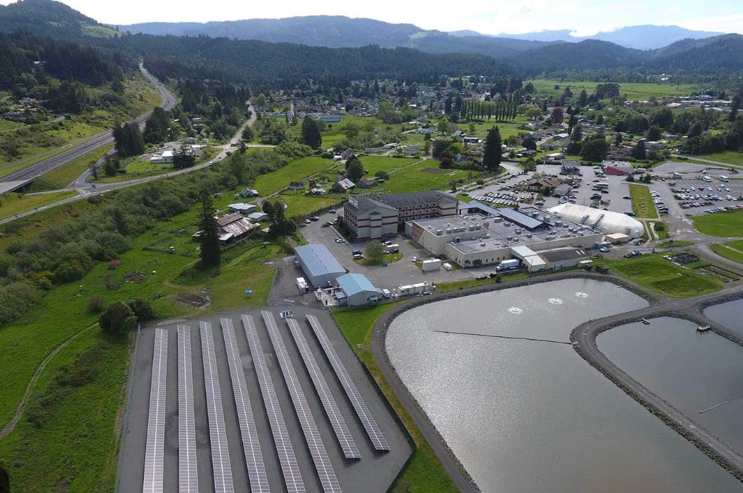 Aerial view of the Blue Lake Rancheria, showing the rows of solar panels that anchor the Tribe's microgrid beside the casino and hotel complex, with forested hills beyond.