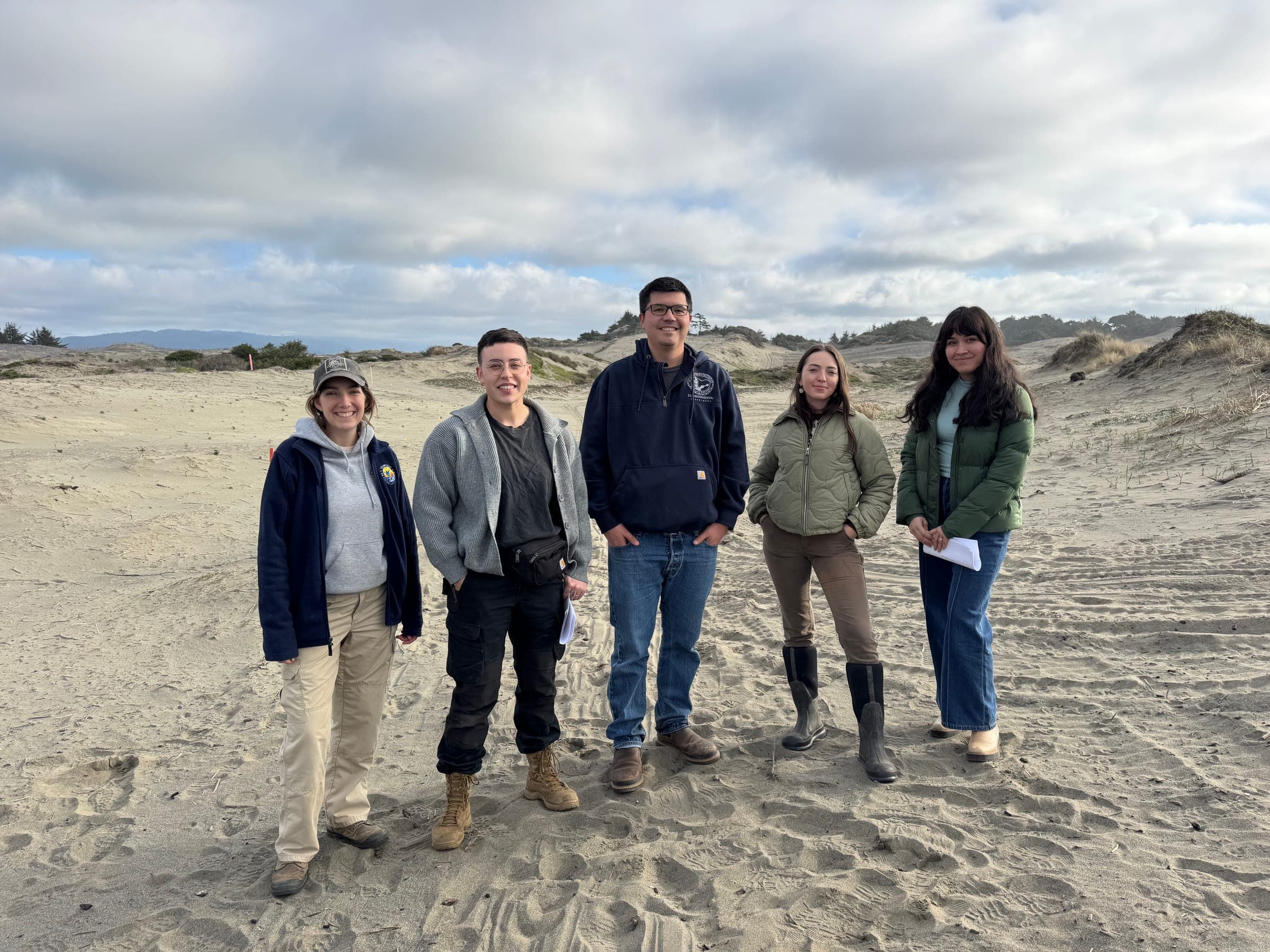 Five members of the restoration crew standing together on the coastal dunes where the team carries out native seed collection and restoration work.